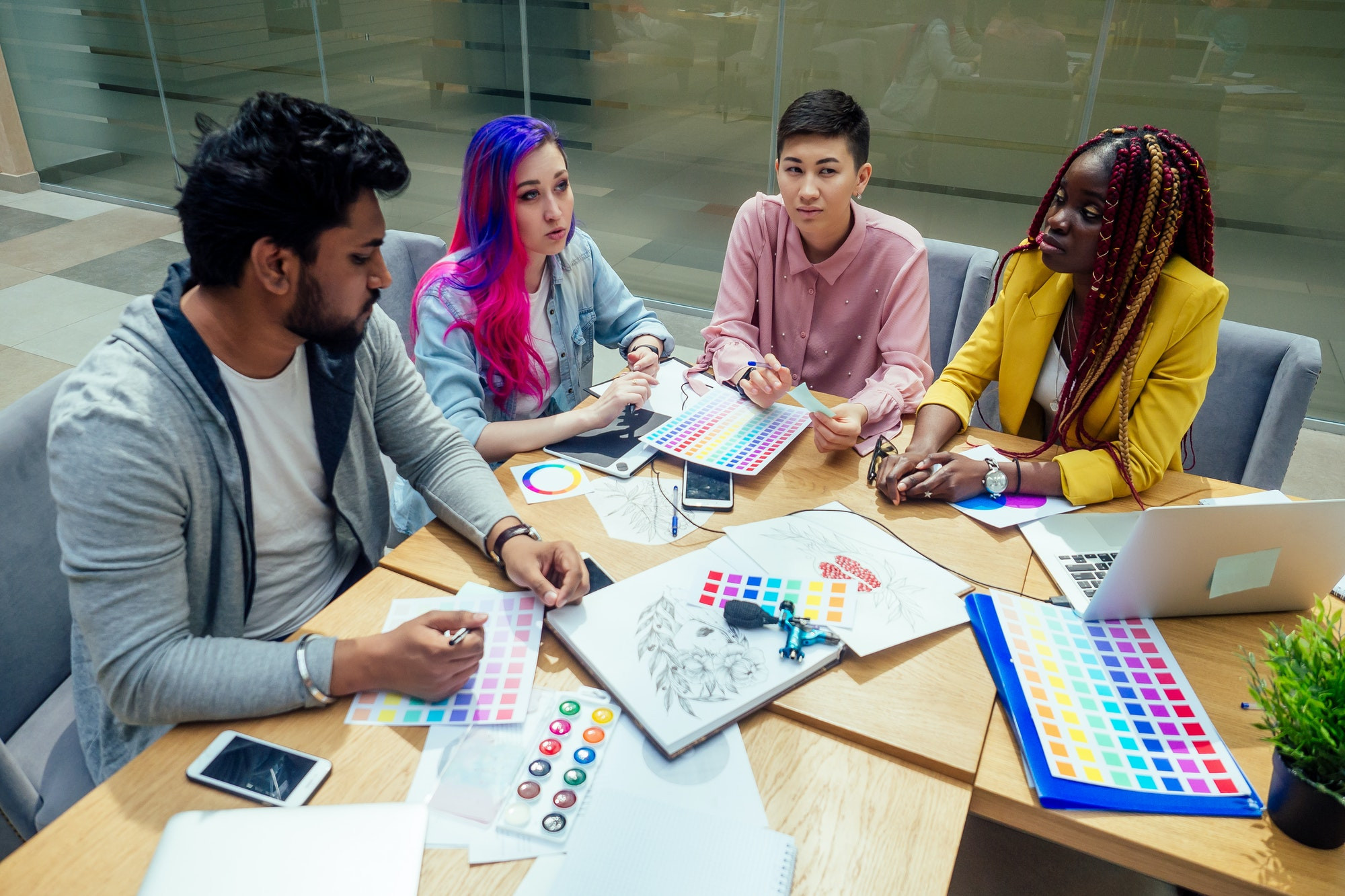 équipe de créateurs d'agence créative travaillant ensemble : femme afro-américaine avec des tresses de dreadlocks et fille caucasienne rose bleu cheveux multicolores communication avec un homme indien au bureau.